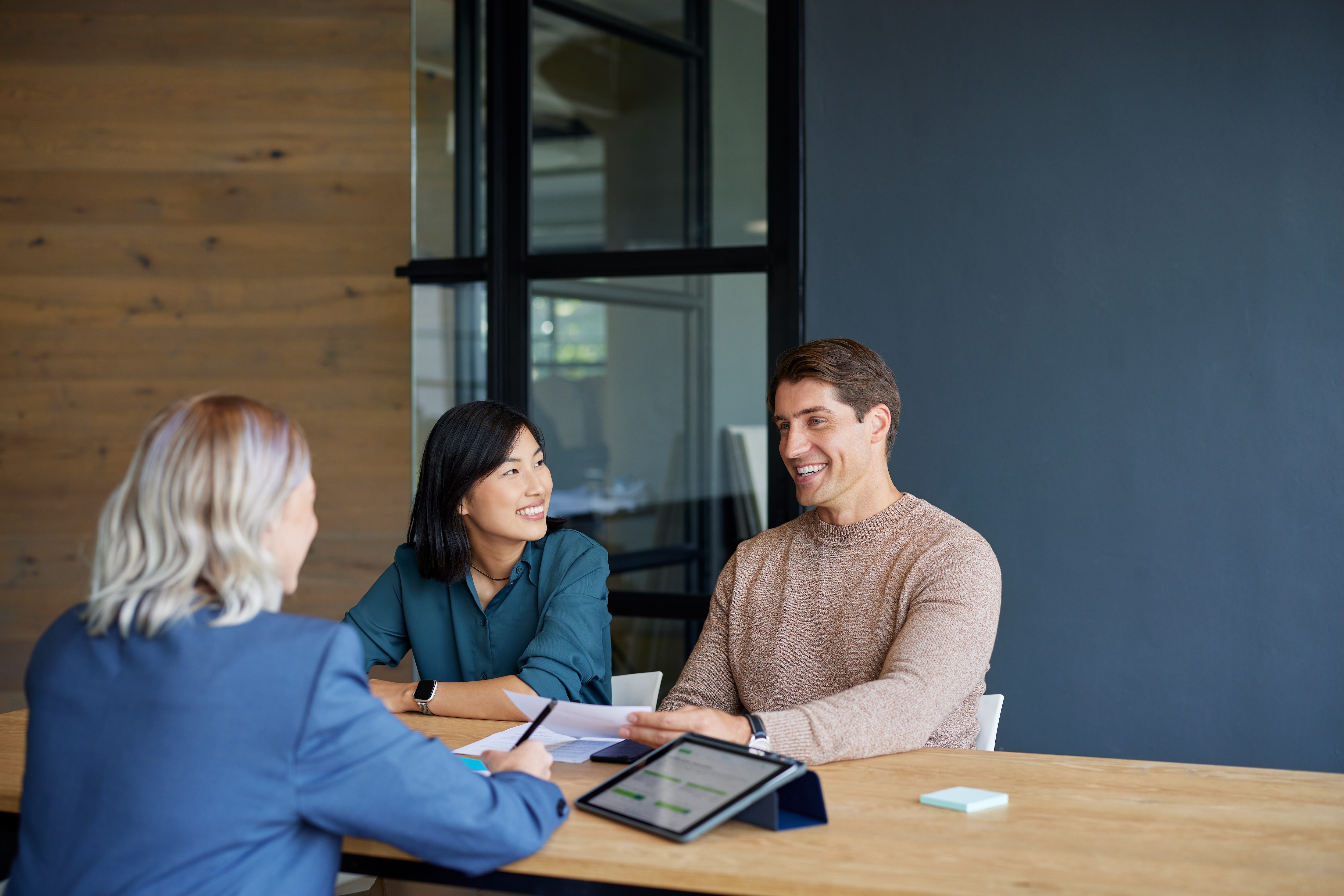 A man and woman happily sit at a desk across from an advisor. 