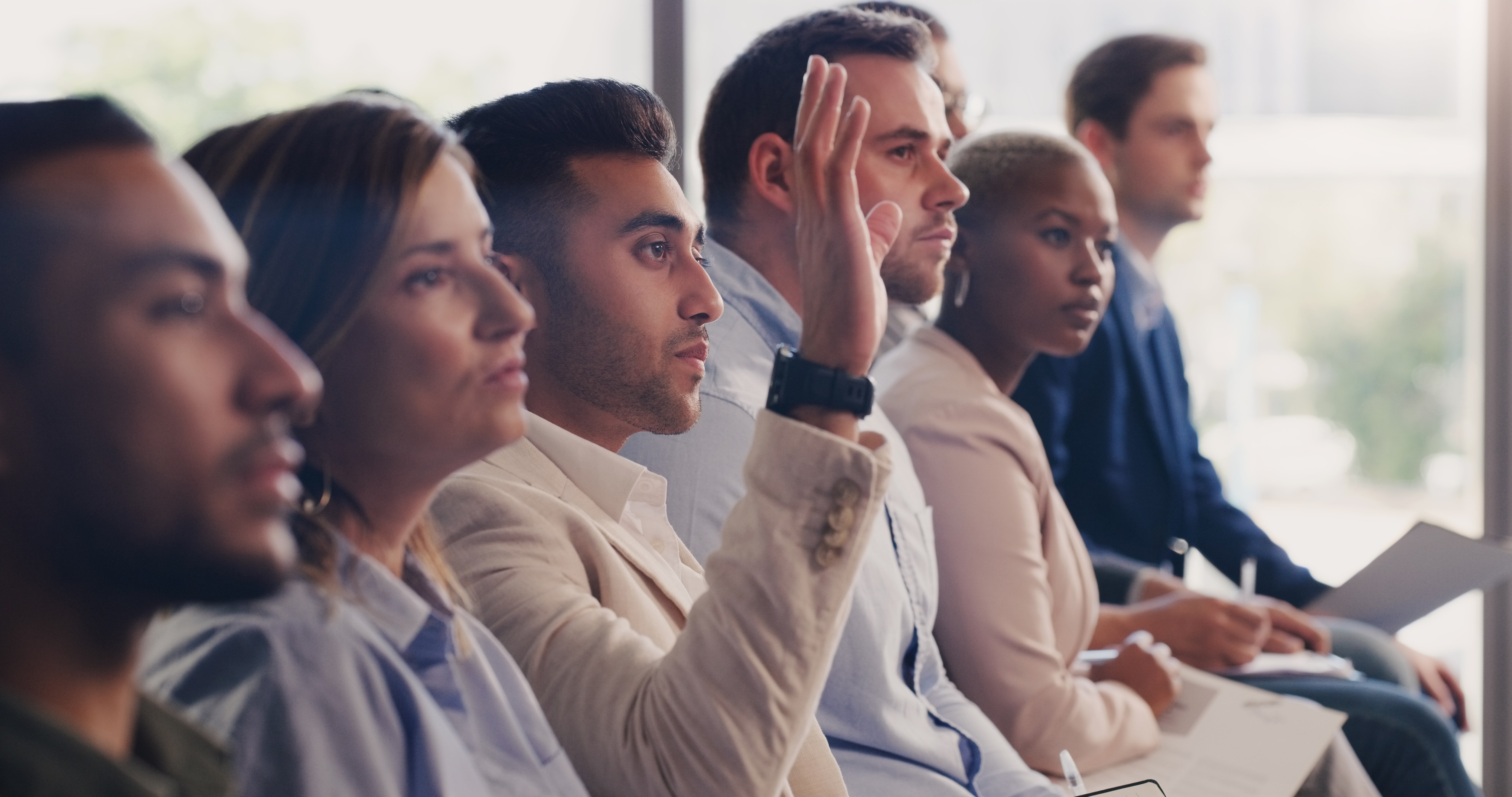 Audience, conference and question of a business man with hand up at a seminar, workshop or training. Diversity men and women crowd at a presentation for learning, knowledge and faq discussion.