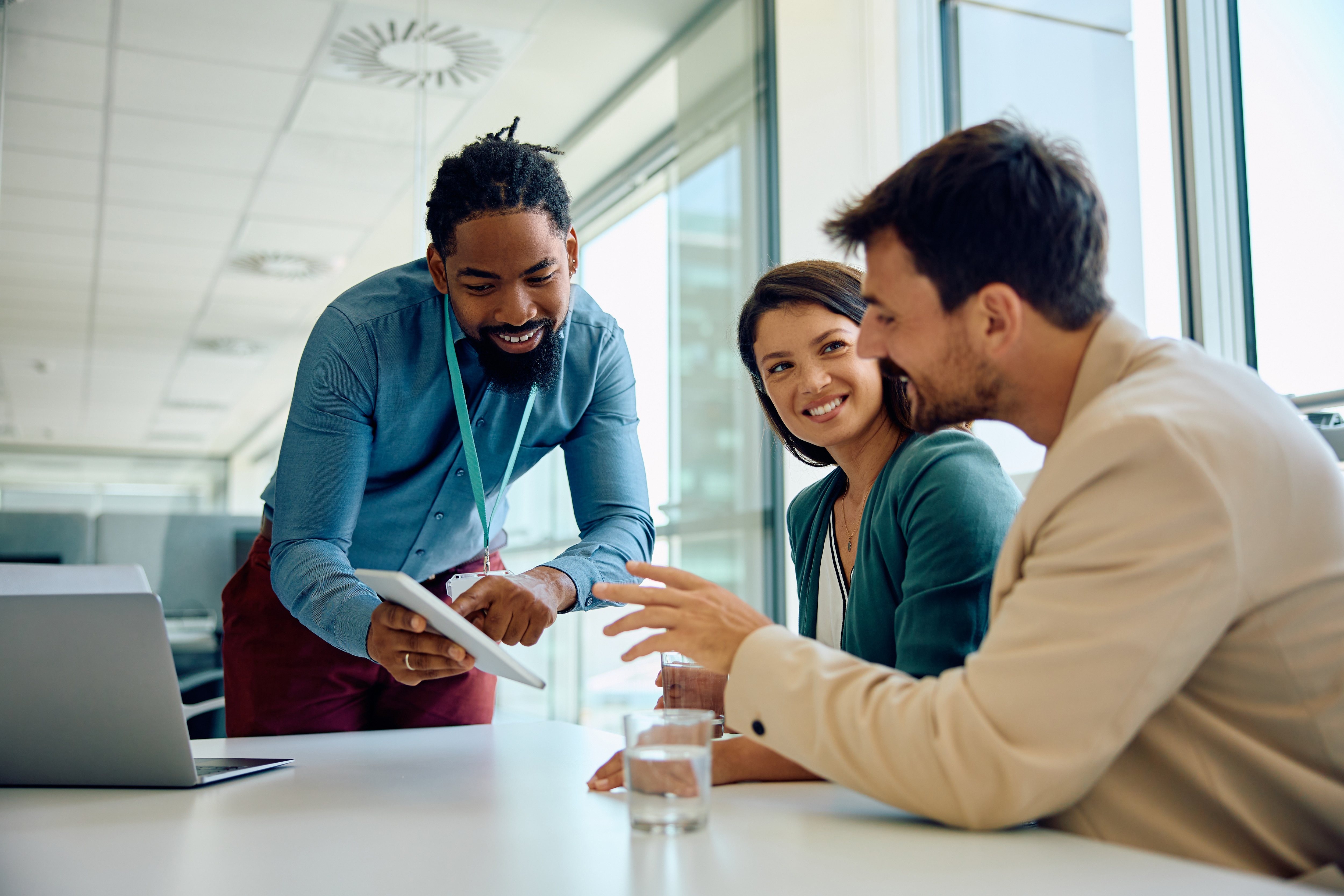 Happy black financial advisor using touchpad with his clients during meeting in office. 