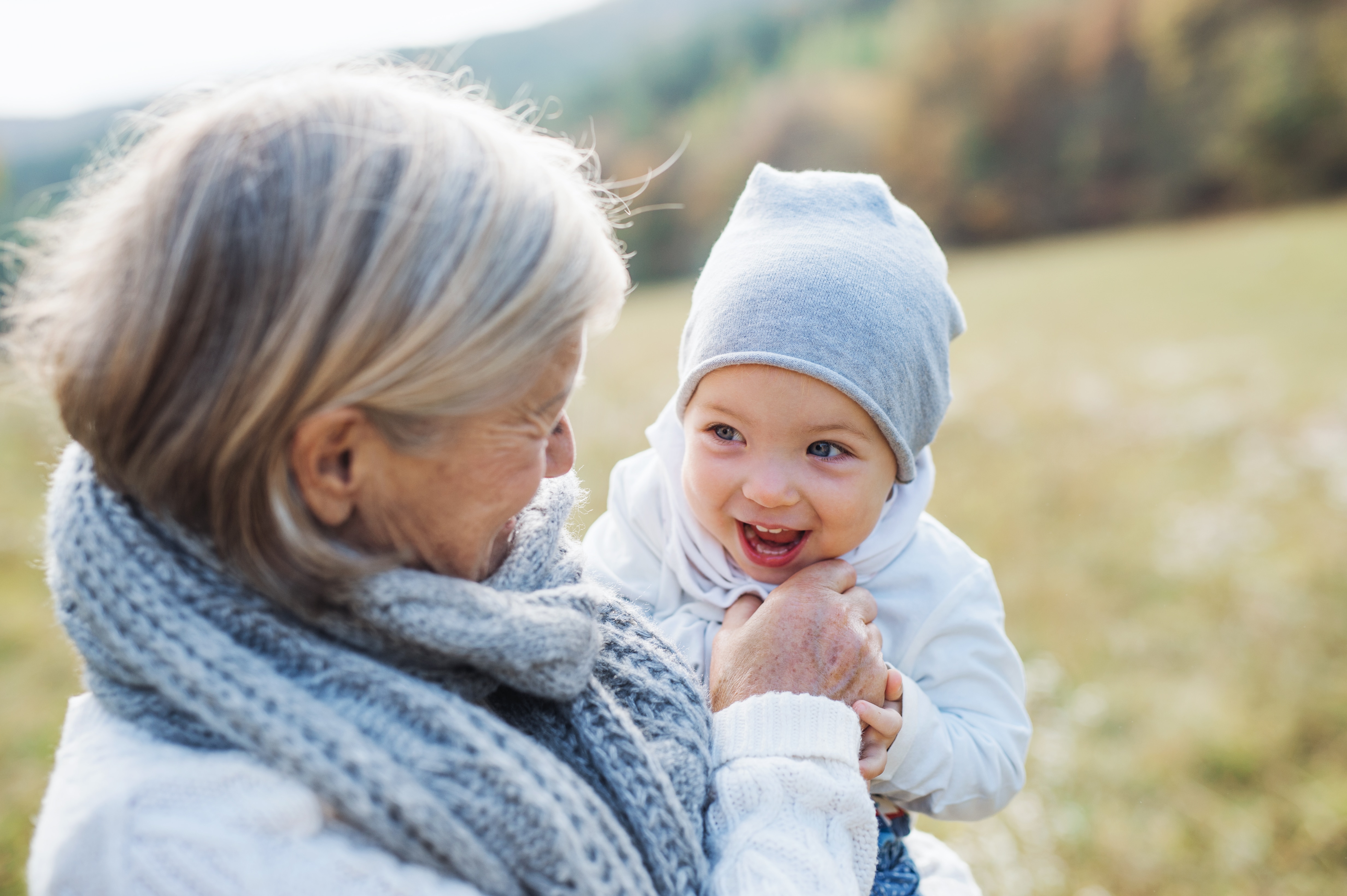 Small toddler spending time with her grandmother outside on a meadow in autumn.
