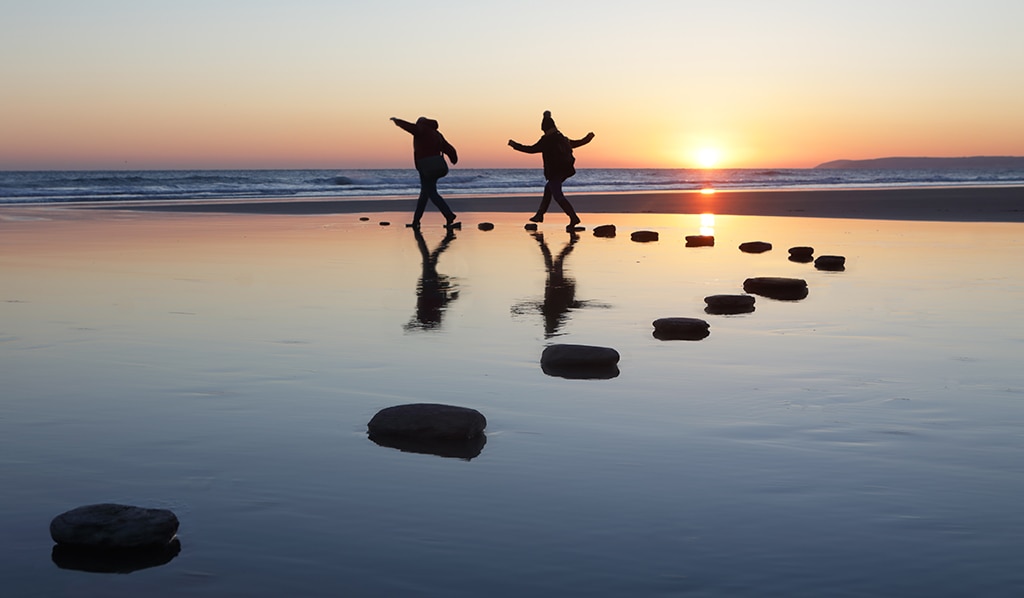 Silhouettes of children playing on stepping stones at sunset