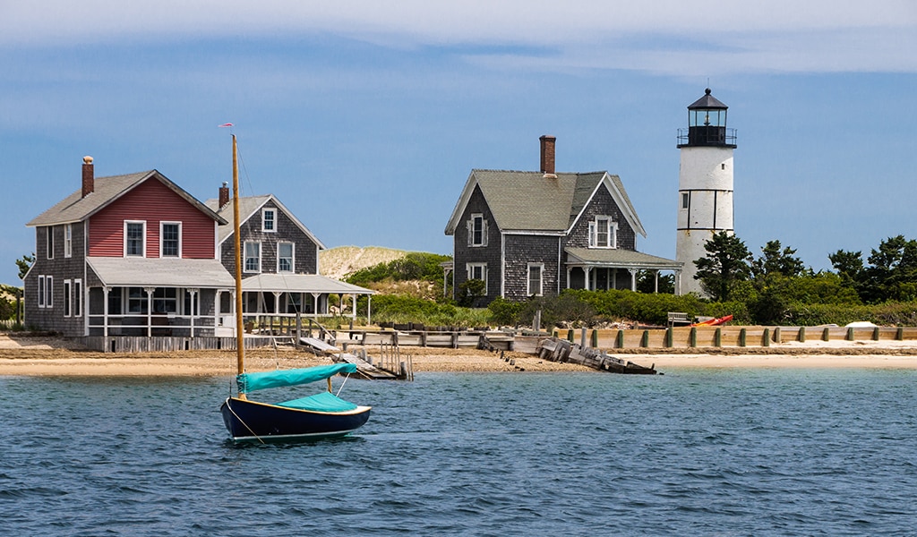 Sailboat, dock, and seaside cottages with lighthouse in the distance