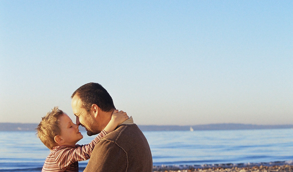 Father and young son rubbing noses by seaside