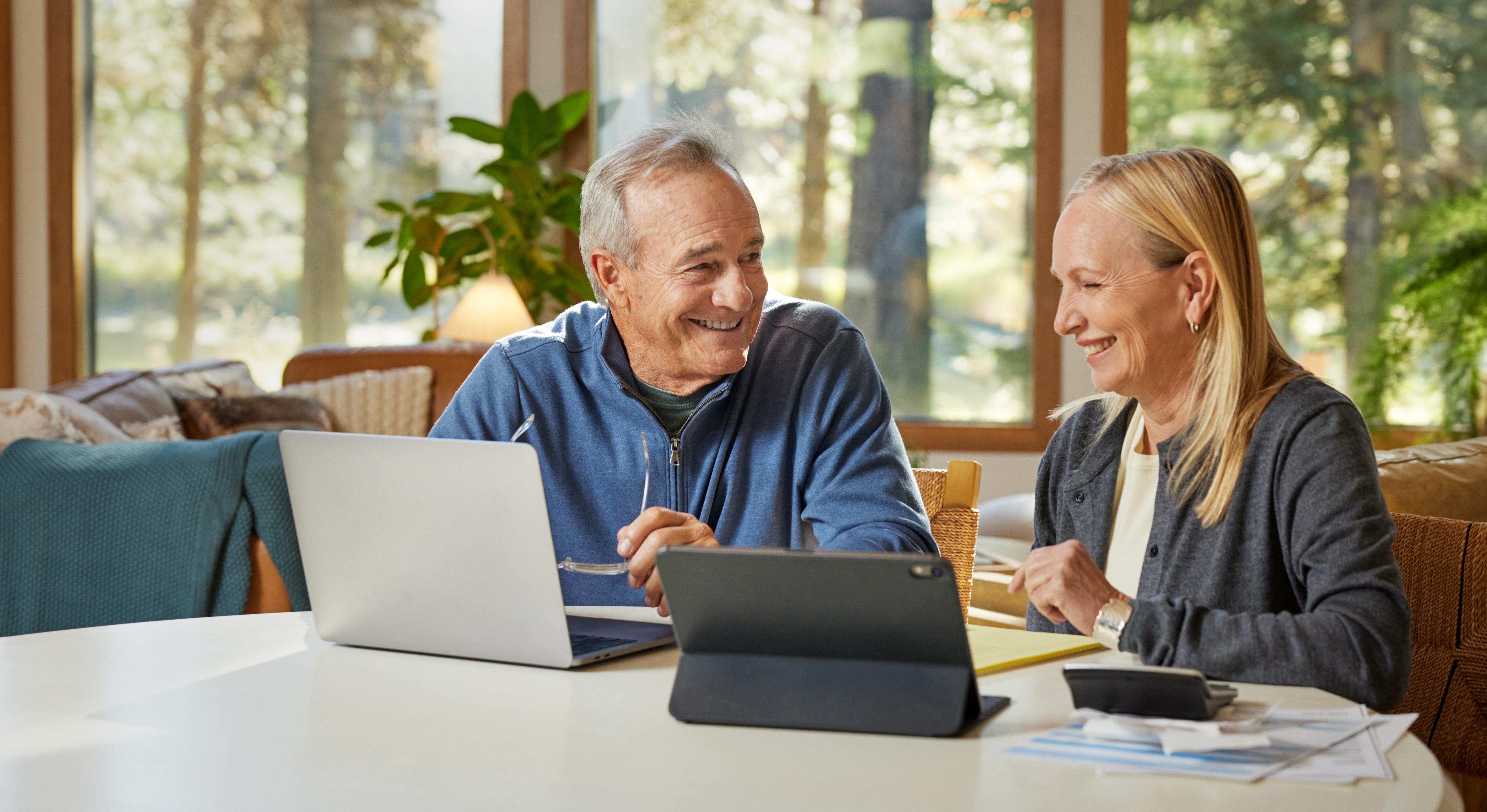 man and woman smiling and looking at a laptop and ipad