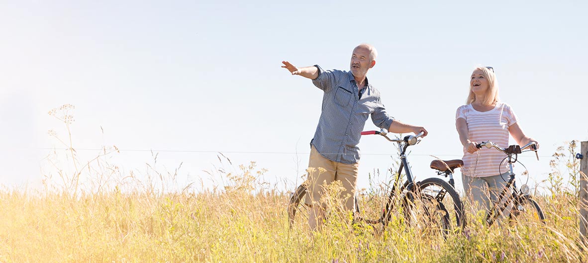 alt=Couple riding bicycles through an open field.